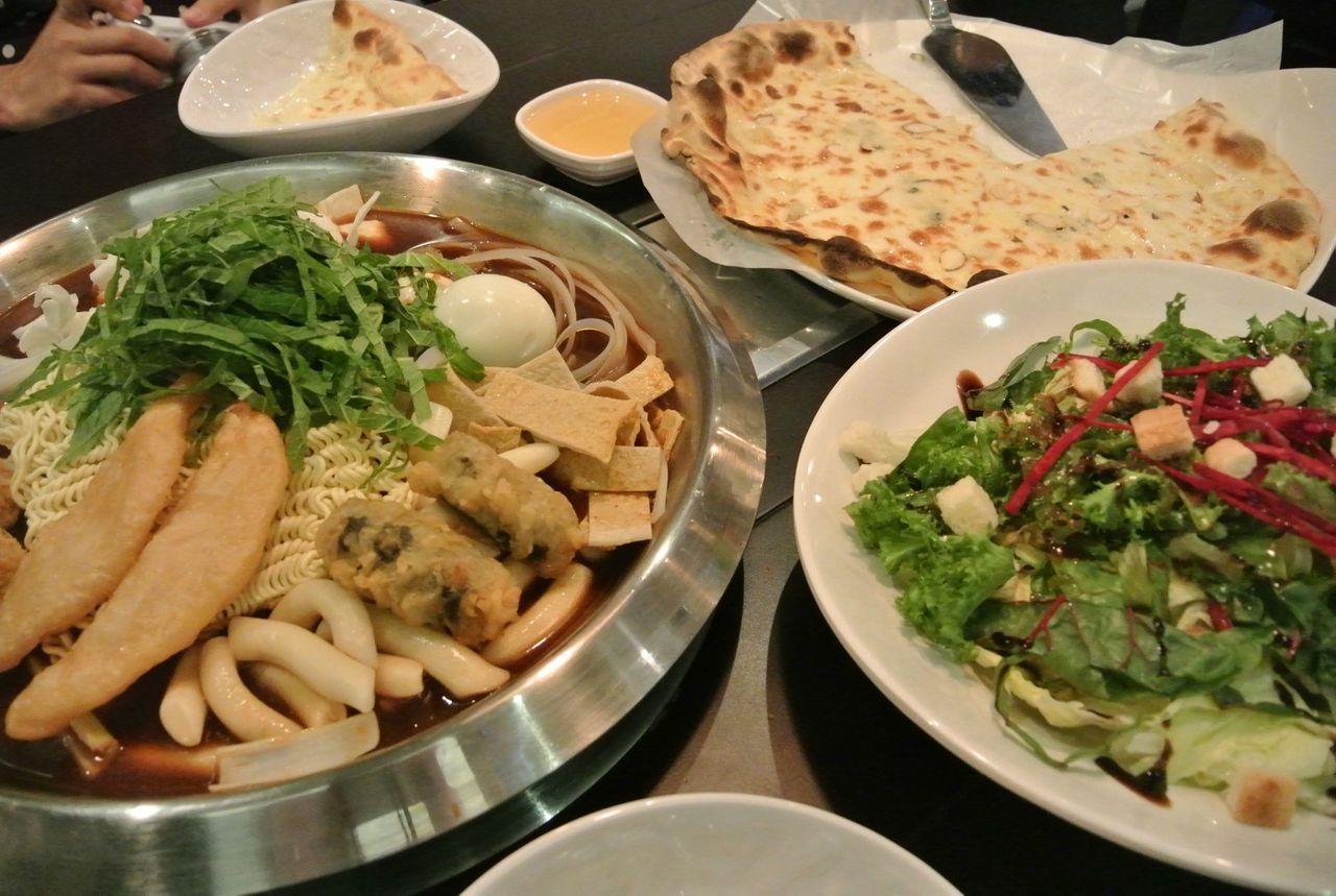 Table spread at Hwa Tteok featuring instant Tteokbokki set and crunchy green salad, illustrating a mix of Korean flavors.